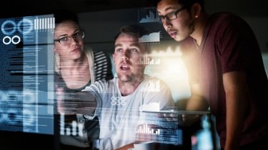 Three colleagues gathered around a computer screen, sharing insights and ideas.